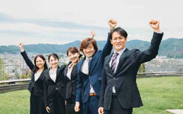 スーツ姿の男女が手を挙げている写真