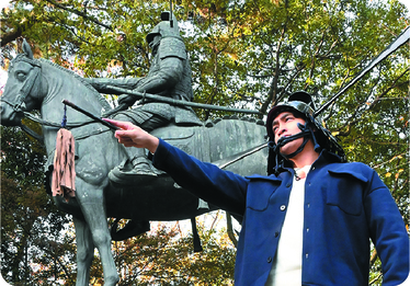 藤堂高虎像の前でポーズをとる佳久創さん